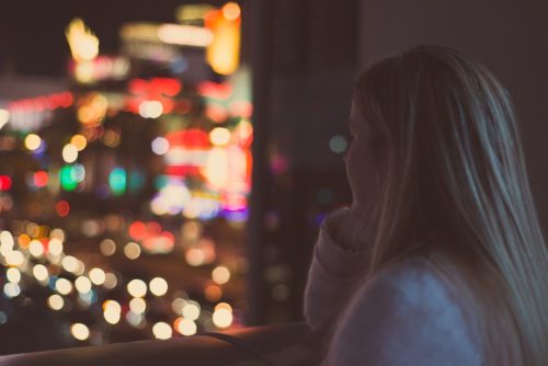 A contemplative woman gazes out at a city nightscape, enveloped in a symphony of vibrant, unfocused lights.
