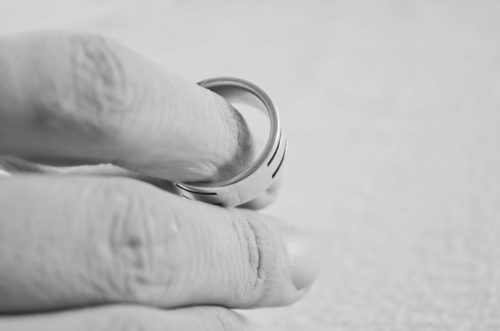 A close-up in grayscale of a person's fingers holding a silver band, possibly symbolizing contemplation or memories related to commitment or marriage.