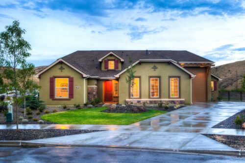 Suburban home at dusk with illuminated windows, a well-manicured lawn, and a welcoming walkway under a cloudy sky, not far from where one might seek a divorce lawyer near Nassau County