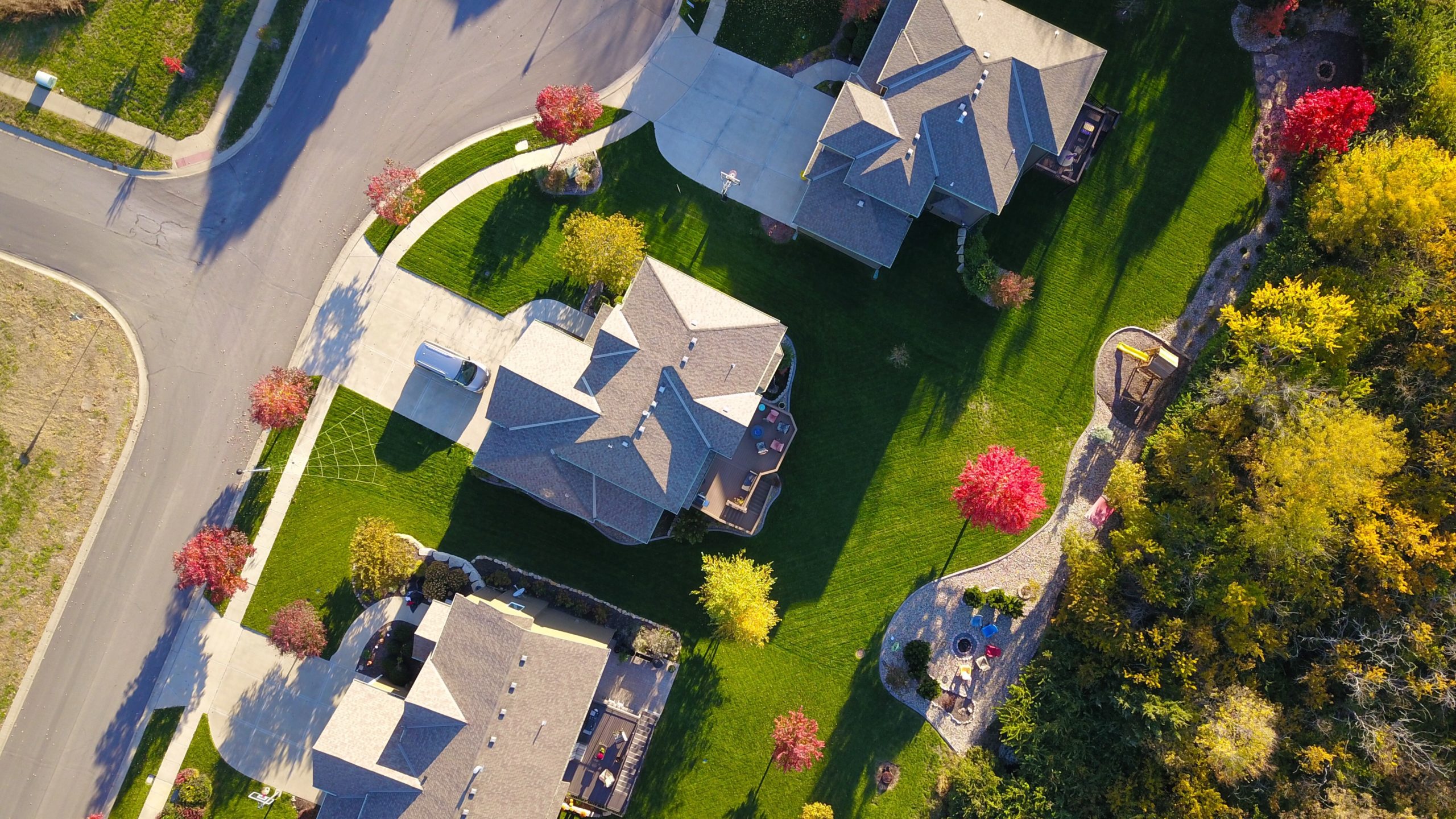 Aerial view of a suburban neighborhood in autumn, showcasing the sprawling lawns and the vibrant colors of the foliage around cozy single-family homes, near a reputable firm known for handling same-sex divorce cases in