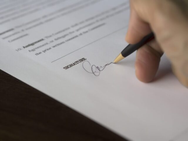 Finalizing a prenuptial agreement: a person signs their name on a contractual document with the advice of a Long Island Prenuptial Agreement Lawyer.