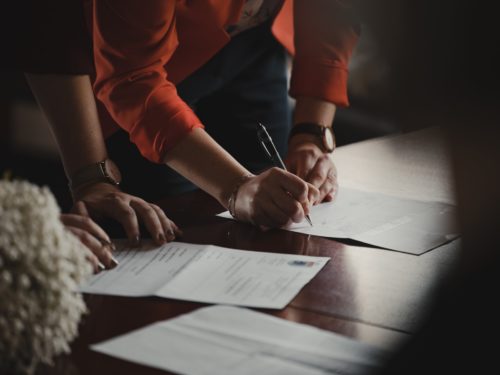 Close-up of two individuals at a table with documents, one person is using a pen to sign or fill out a form, suggesting a formal agreement or business transaction in progress with same sex divorce lawyers in