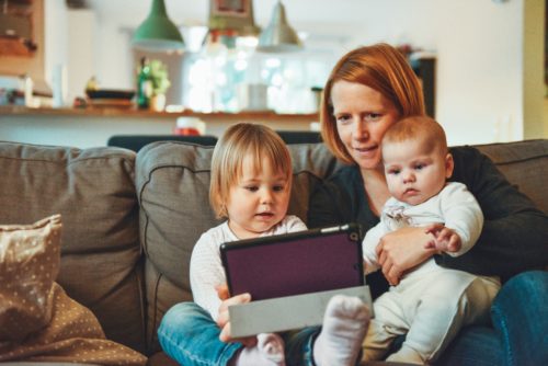 A mother sitting on a sofa with her two young children, engaging with a tablet together in a cozy home environment, considering consulting a divorce lawyer from Smithtown.