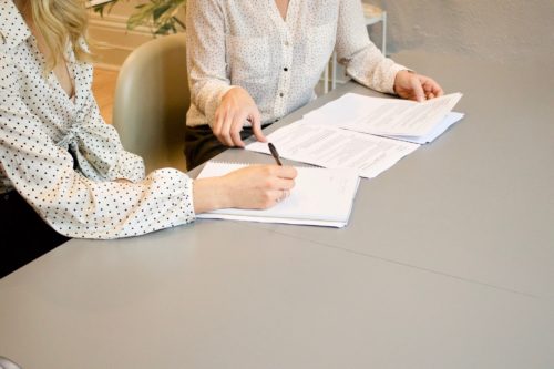 Two individuals engaged in a review or signing of divorce documents at a table, focusing on the task at hand with papers and a pen.