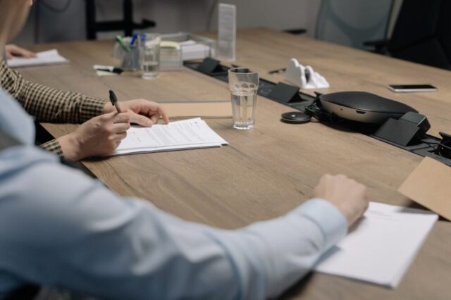 Two individuals, possibly Jewish divorce lawyers, engaged in paperwork at a modern office table, in the midst of a business meeting or collaboration.