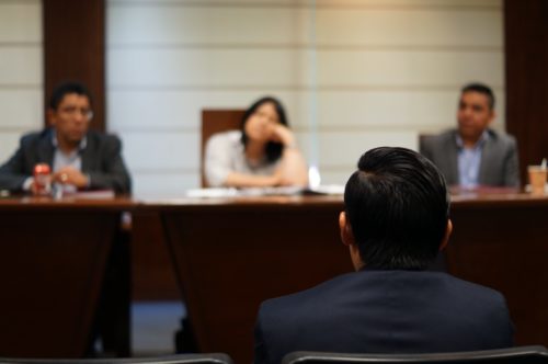 A person presenting to a panel of three listeners in a formal meeting setting, with focus on the divorce lawyer's back and the panel slightly out of focus.