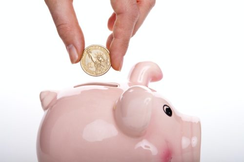 A hand inserting a coin into a pink piggy bank, symbolizing savings and financial planning for permanent alimony in NY.