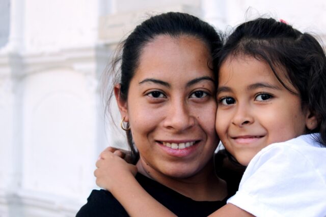 A tender moment captured as a smiling woman tenderly hugs a young girl, their close bond evident in their warm and happy expressions, despite the challenges faced during the same-sex divorce proceeding in New York.