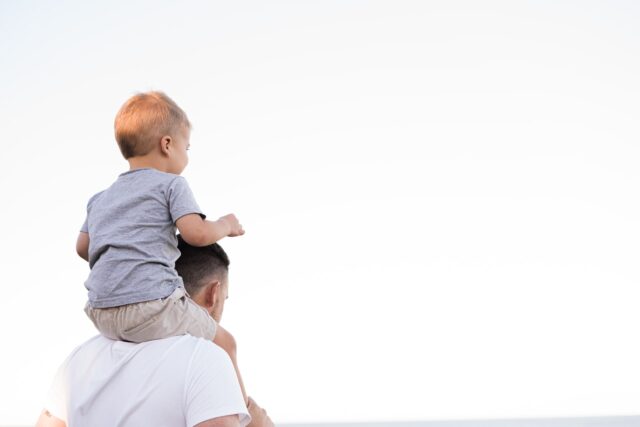 A young child, whose parents are engaging a Long Island child support lawyer, sits high on an adult's shoulders, both gazing into a clear horizon.