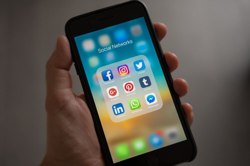 Hand holding a smartphone with a screen displaying social media apps in a folder labeled 
