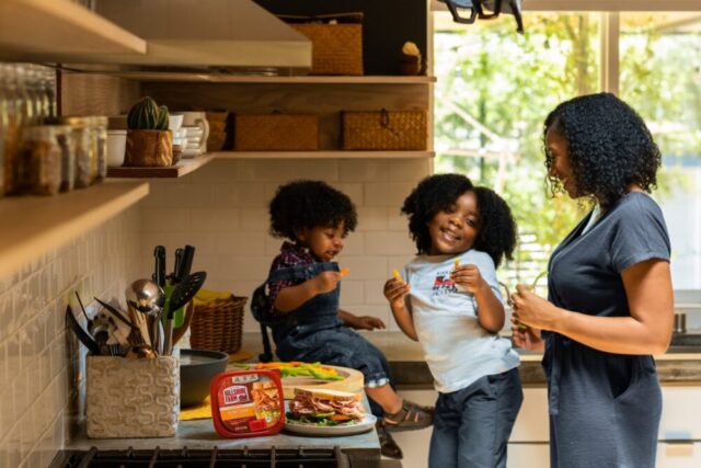 A joyful family moment in a warm kitchen as a mother shares a laugh with her two young children while preparing a meal together, embodying the unity and love that remains paramount despite navigating through the complexities of