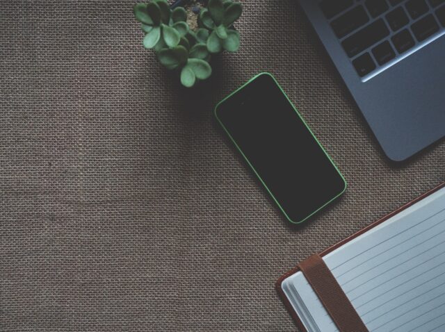 A modern workspace featuring a smartphone with a neon green outline, a potted plant, and an open notebook beside a laptop on a textured canvas surface, ideal for consultations with a divorce lawyer in Smithtown