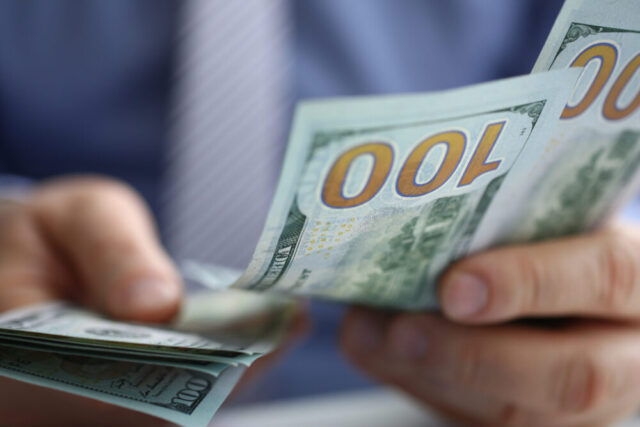 A close-up of an individual counting a stack of US 100 dollar bills for alimony payments.