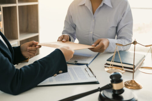 A client handing over a document to a Jewish divorce lawyer in a formal setting, with a gavel and the scales of justice in the foreground, symbolizing the practice of law.
