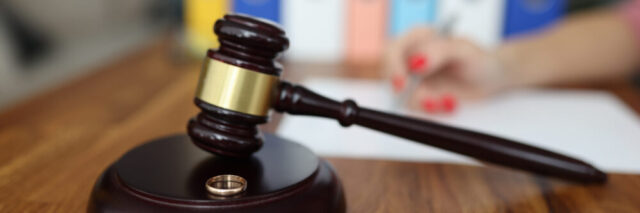 A wooden gavel and a gold-colored band on a sounding block, set on a table with a blurred background of a Long Island child support lawyer writing on paper, symbolizing legal proceedings or the