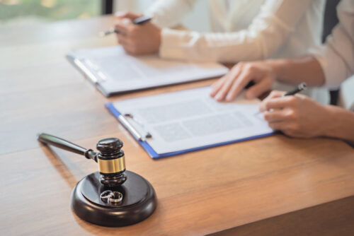 Two individuals reviewing a divorce settlement agreement at a desk with a gavel in the foreground, suggesting a legal or judicial setting.