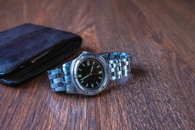 A classic wristwatch beside a folded leather wallet on a wooden surface, reminiscent of the meticulous preparation by a Long Island child support lawyer for their day in court.