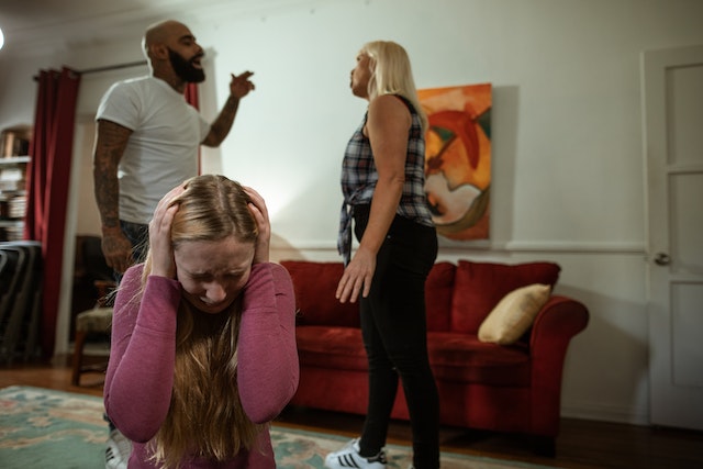 two adults yelling in front of cowering child