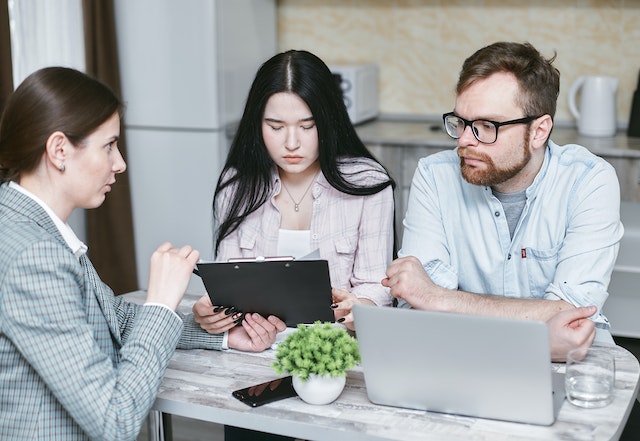 couple sitting at table in front of woman holding clipboard