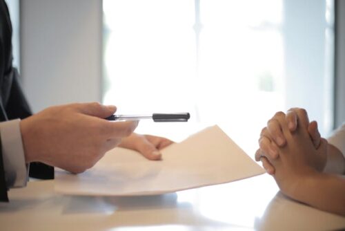 person handing pen and paper to other person