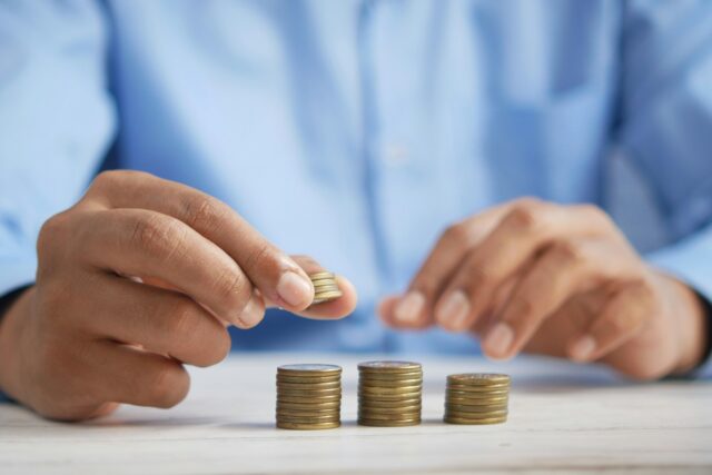 A person in a blue shirt stacks coins into neat piles on a white table, suggesting saving or managing money—much like organizing finances for a financial disclosure during a New York divorce.