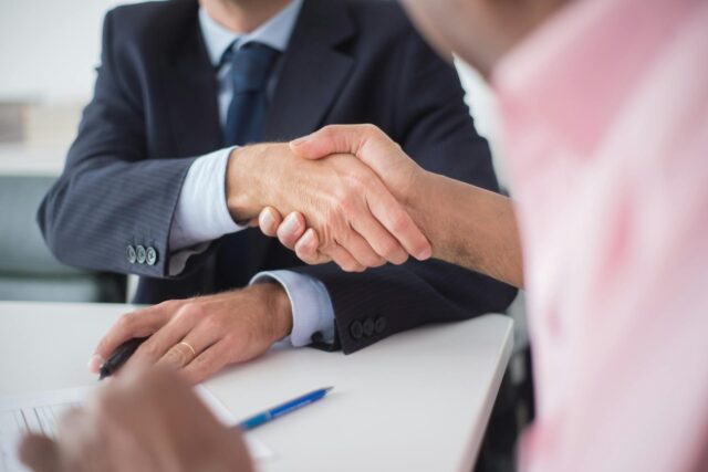 Two people are shaking hands across a desk, finalizing an agreement. A pen and probate documents lie on the table, suggesting they are filing probate in New York in a professional setting.